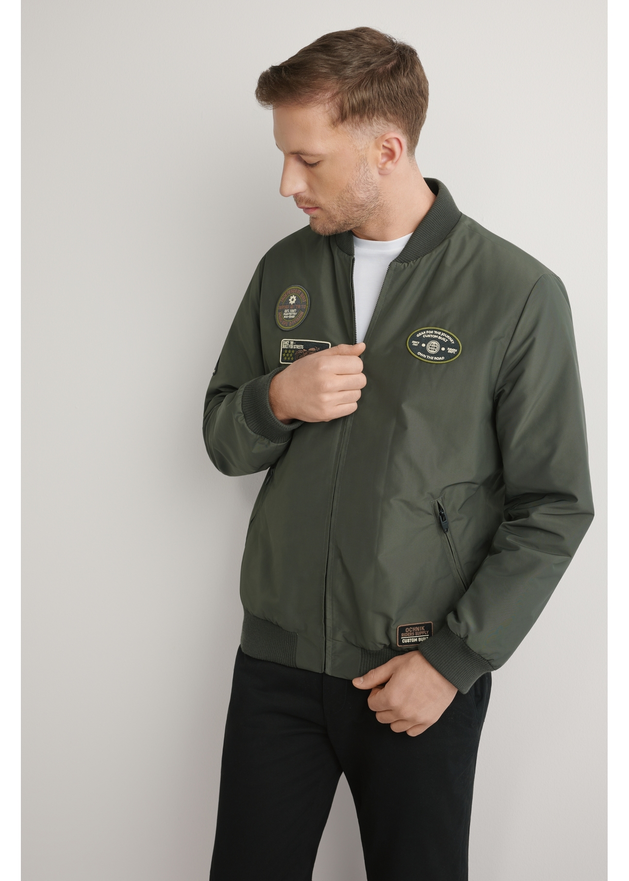 Kurtka bomberka męska w kolorze khaki KURMT-0413A-8D(W26) - widok produktu z przodu na, na jasnym tle. Widoczna połowa sylwetki. 
