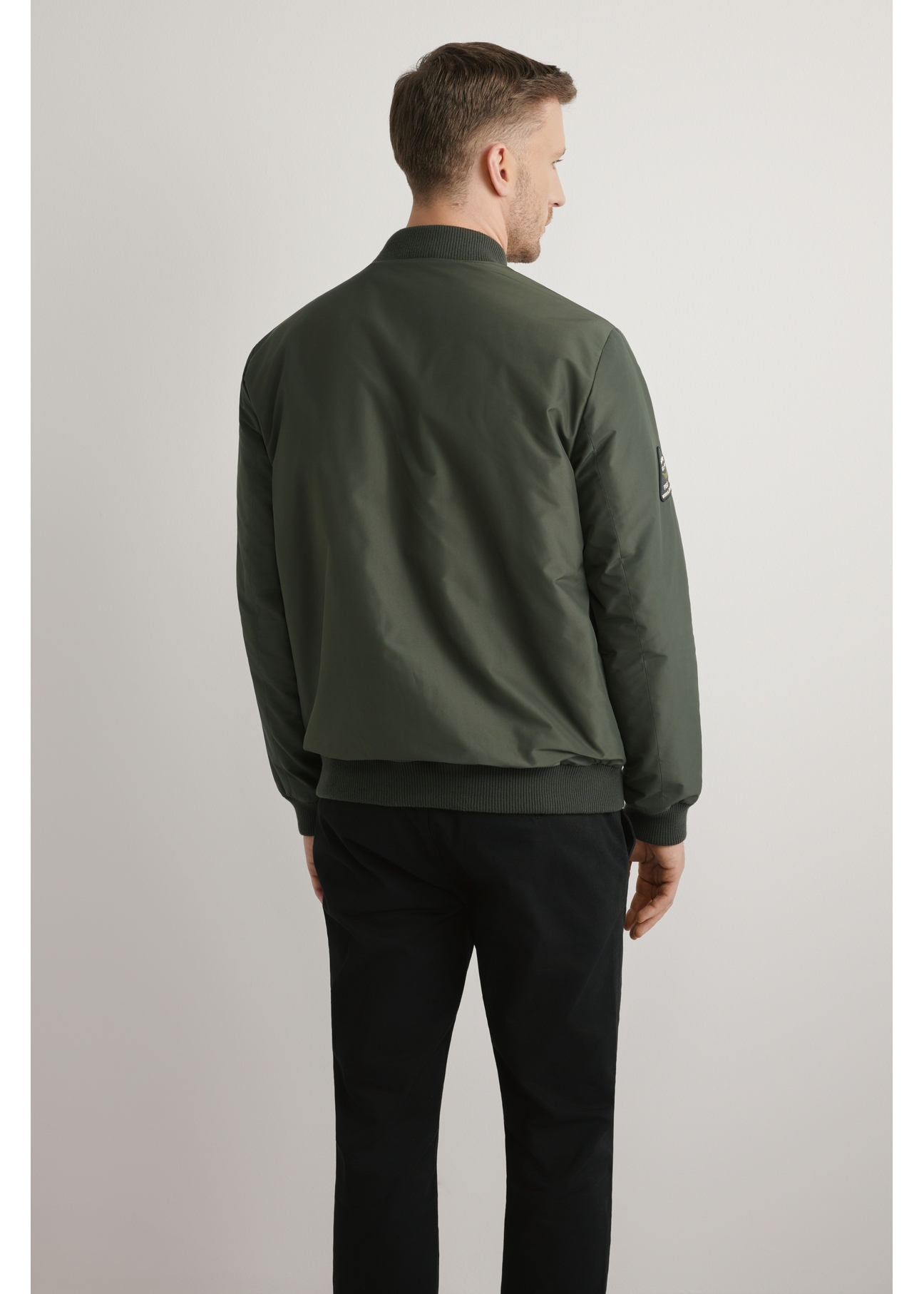 Kurtka bomberka męska w kolorze khaki KURMT-0413A-8D(W26) - widok produktu z tyłu na, na jasnym tle. Widoczna połowa sylwetki. 