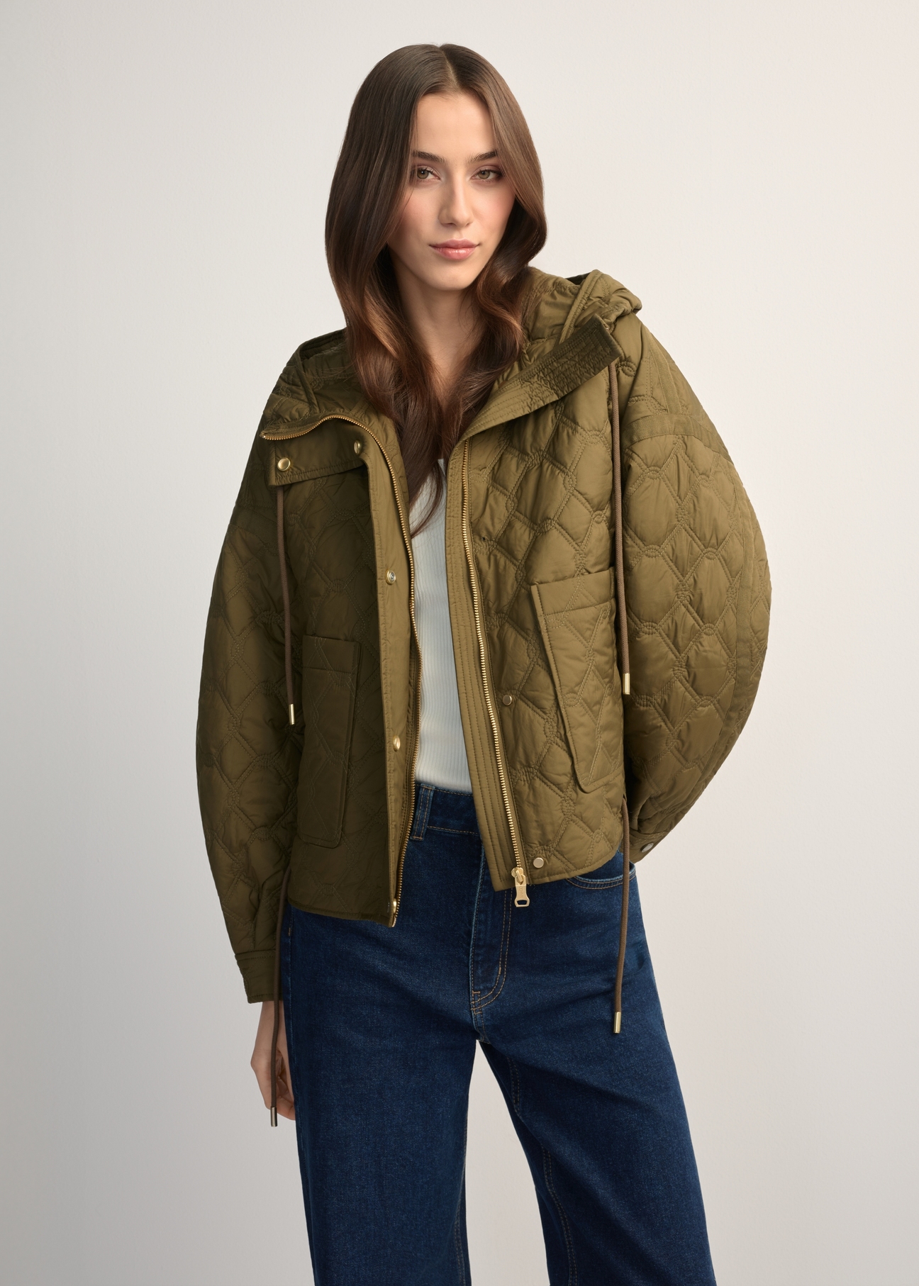 Oliwkowa krótka pikowana kurtka oversize KURDT-0660-8D(W26) - widok produktu z przodu, na modelce, na jasnym tle. Widoczna połowa sylwetki. 