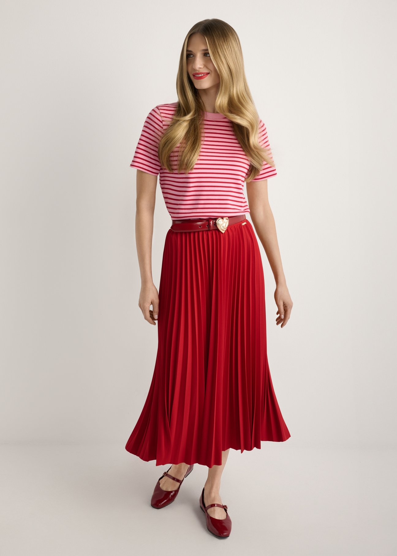 Czerwona plisowana spódnica midi SPCDT-0096-4B(W26), widok produktu od przodu na modelce, widoczna cała sylwetka.
