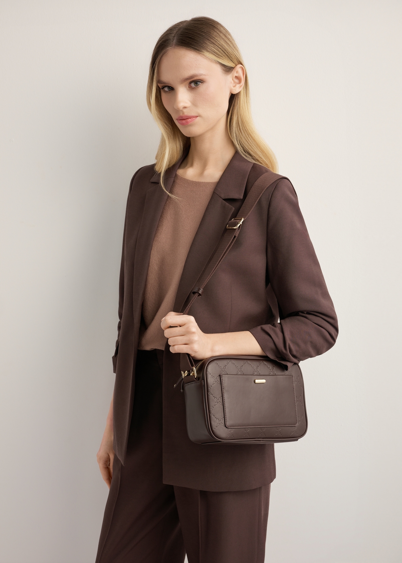 Brązowa torebka damska z monogramem TOREC-1290-1I(Z26), widok skosu produktu na modelce. Widoczna połowa sylwetki. 