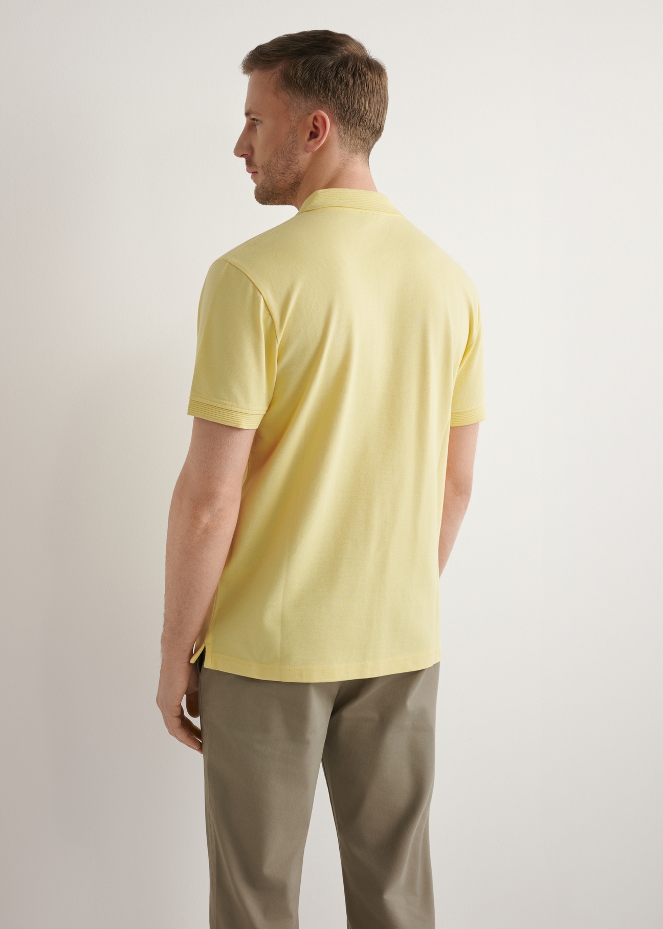 Żółta koszulka polo męska POLMT-0089-2B(W26), widok produktu z tyłu na modelu. Widoczna połowa sylwetki.