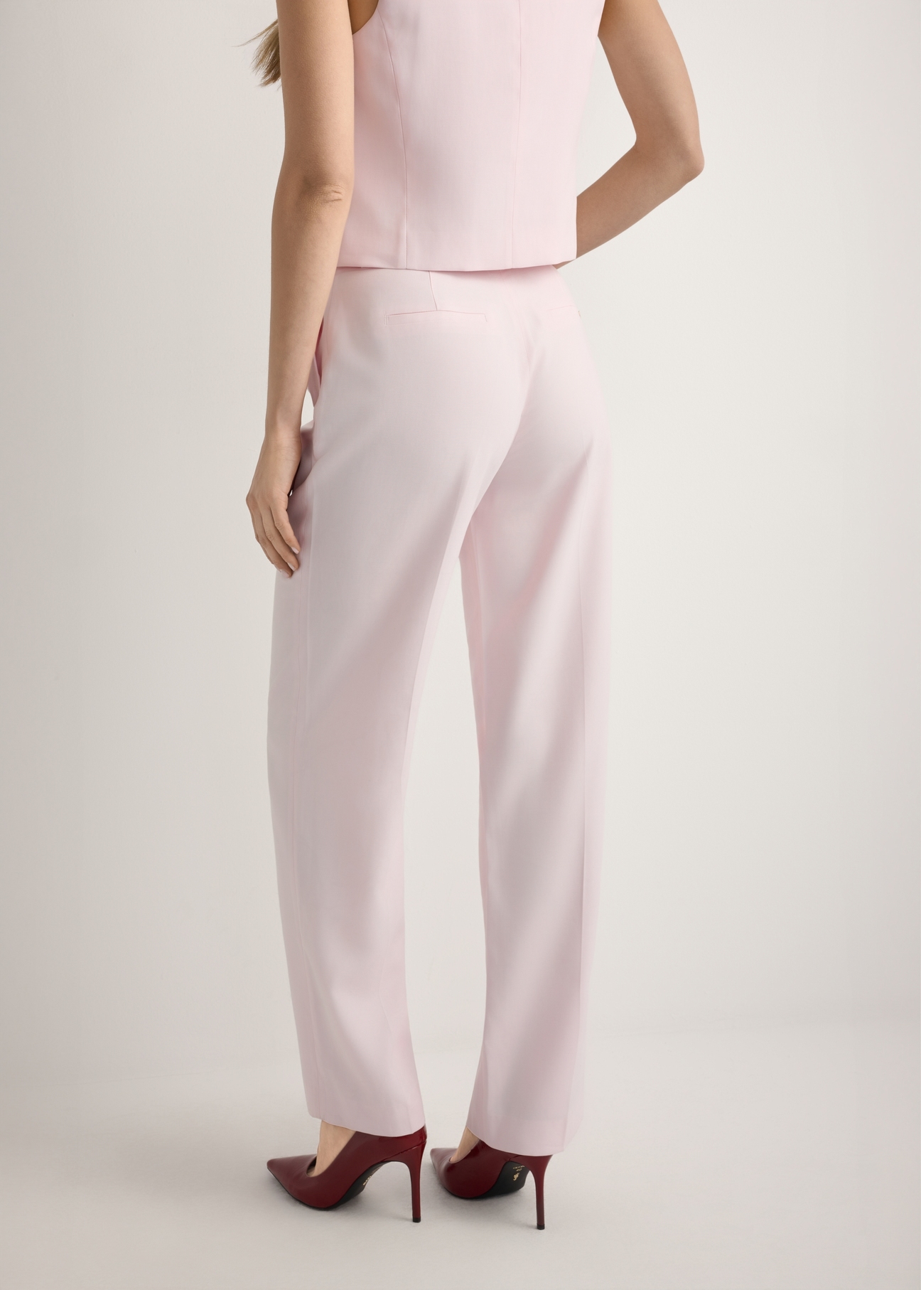 Jasnoróżowe eleganckie spodnie damskie SPODT-0106A-5A(W26), widok produktu od tyłu na modelce, widoczna połowa sylwetki.