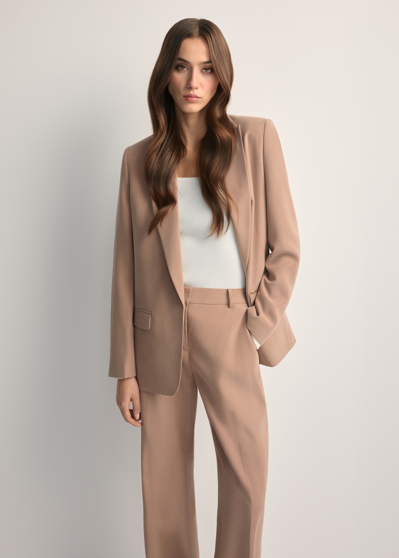Marynarka damska w kolorze camelowym ZAKDT-0031A-1D(W26) - widok produktu z przodu, na modelce, na jasnym tle. Widoczna sylwetka do kolan. 