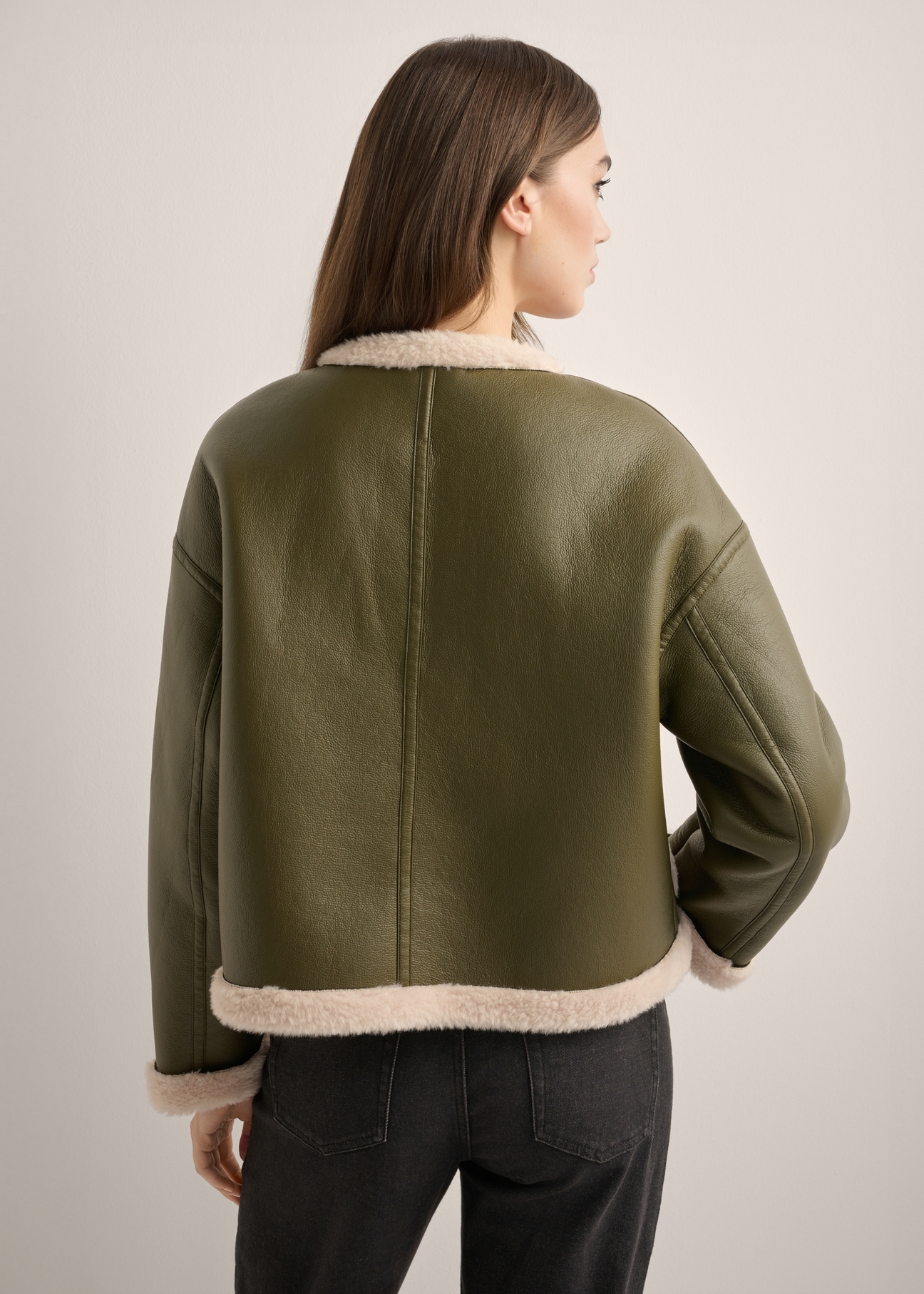 Krótki kożuch damski w kolorze khaki KOZDP-0015-8D(Z26), widok produktu od tyłu na modelce. Widoczna połowa sylwetki.