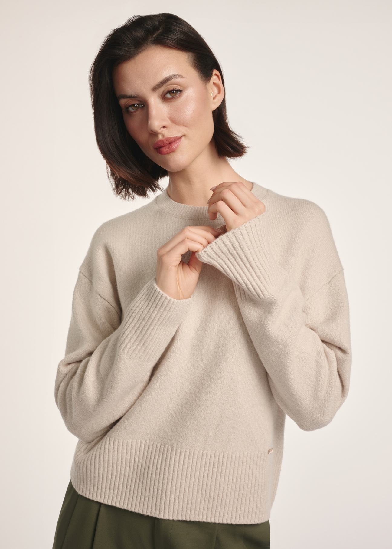 Beżowy sweter damski SWEDT-0242-80(Z25), widok produktu z przodu na modelce. Widoczna połowa sylwetki.