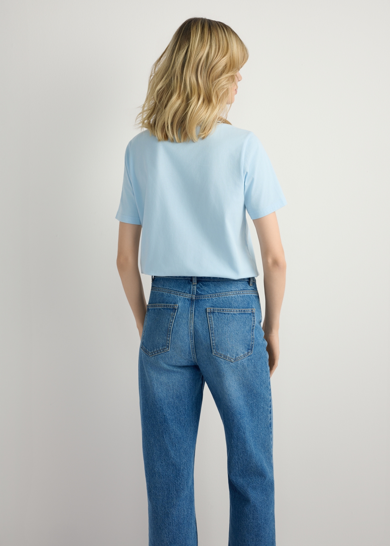 Jasnoniebieski T-shirt damski basic TSHDT-0120-7A(W26), widok produktu z tyłu na modelce. Widoczna połowa sylwetki.