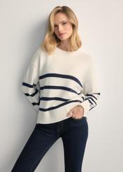 Kremowy sweter damski w paski SWEDT-0258-0B(W26) - widok produktu z przodu, na modelce, na jasnym tle. Widoczna sylwetka do kolan. 