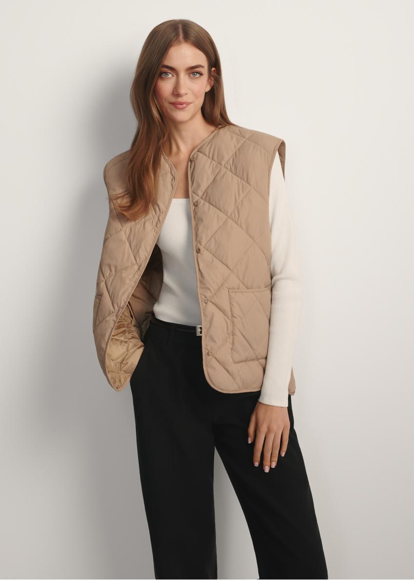 Beżowa pikowana kamizelka damska KAMDT-0035-1C(W26), widok produktu z przodu na modelce. Widoczna połowa sylwetki.